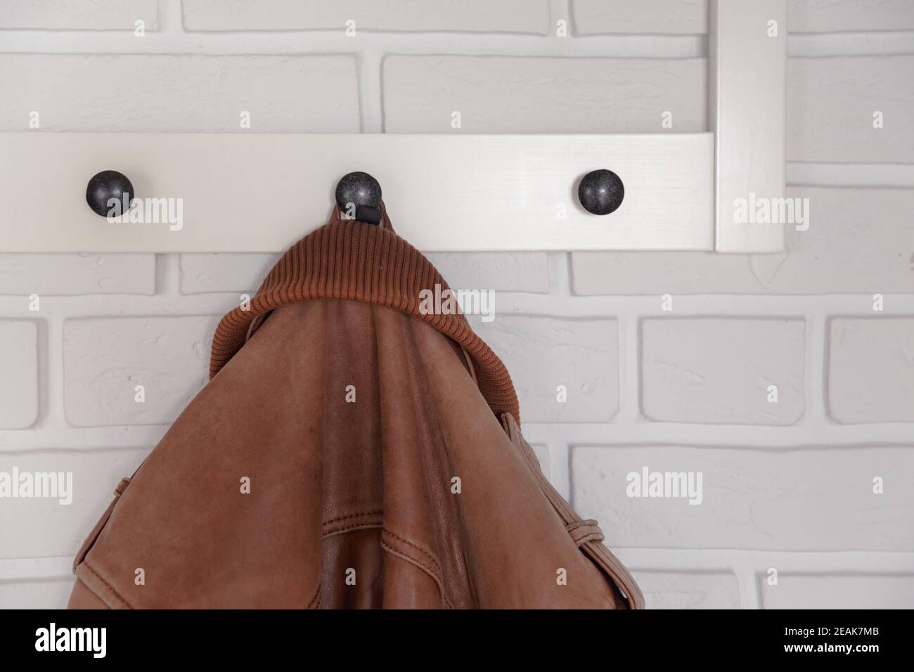 Brown leather jacket hanged on white wall hanger Stock Photo
