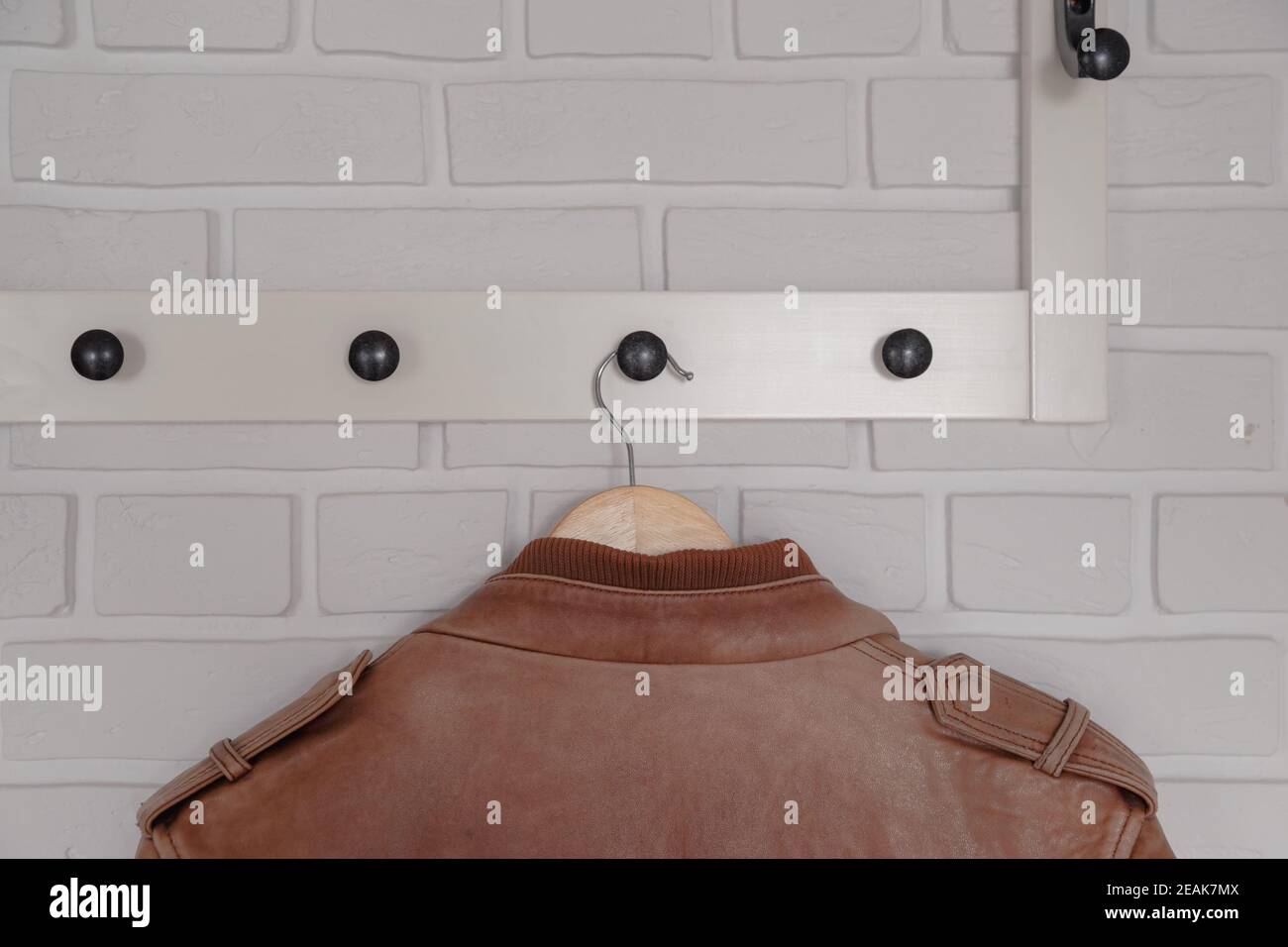 Brown leather jacket hanged on white wall hanger Stock Photo