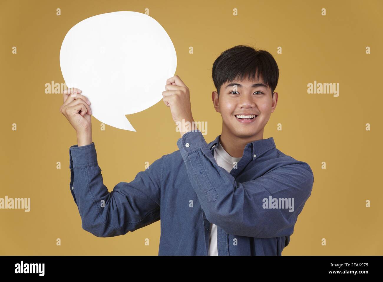 portrait of smiling happy cheerful young asian man dressed casually with empty speech bubble isolated on yellow studio background Stock Photo