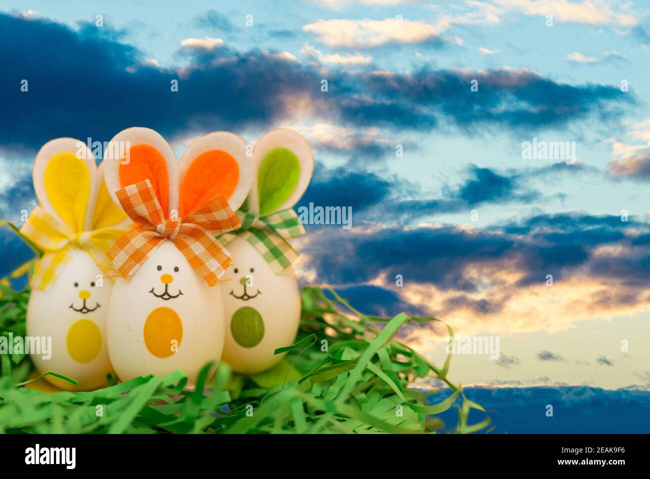 Decorated easter eggs, three bunnies on grass over blue sky sunset cloudy evening background. Happy Easter. Stock Photo