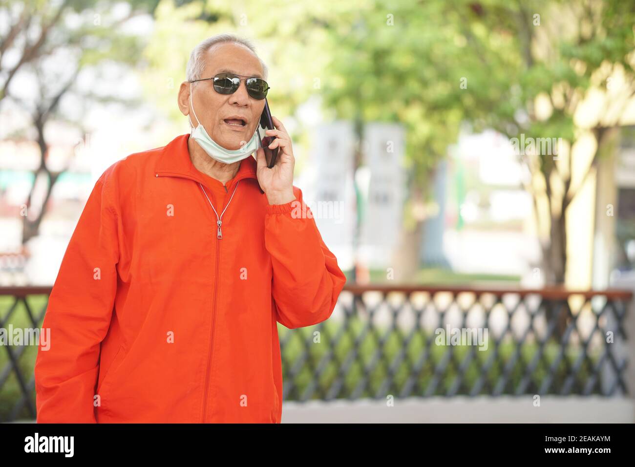 asian old asian elderly senior elder man talking on smart mobile phone outdoor Stock Photo