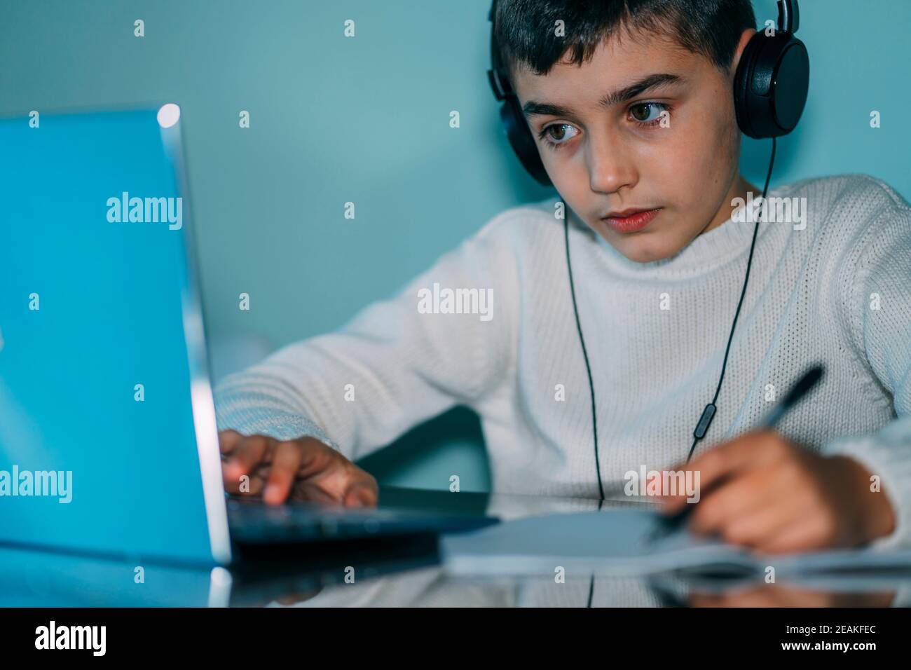child uses laptop computer at home. He wears headphones and uses a