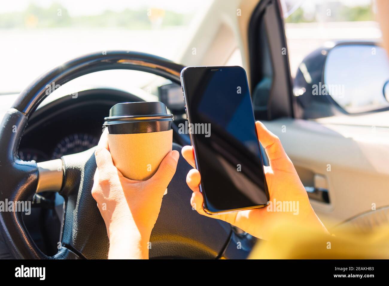 woman drinking hot coffee takeaway cup inside a car and using smartphone Stock Photo