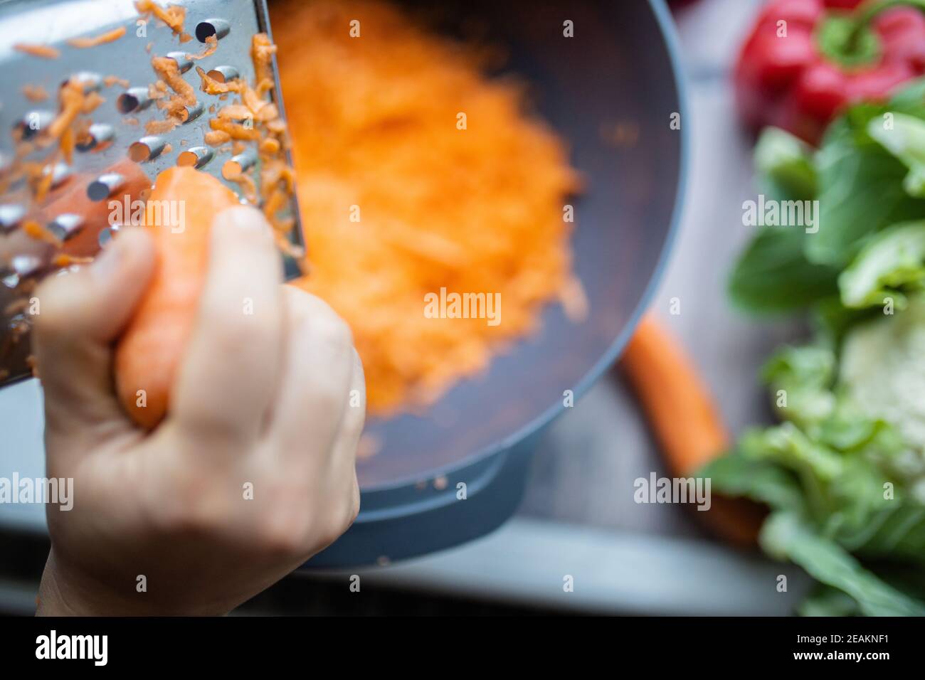 Female hands firmly grating a carrot into a bowl Stock Photo