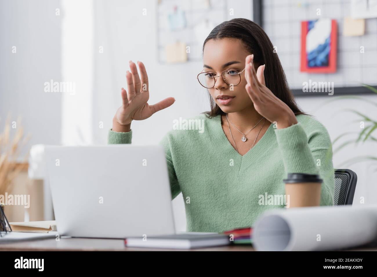 young african american interior designer gesturing while looking at laptop on blurred foreground Stock Photo
