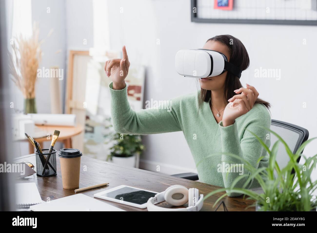 african american freelance architect gesturing while using vr headset at workplace, blurred foreground Stock Photo