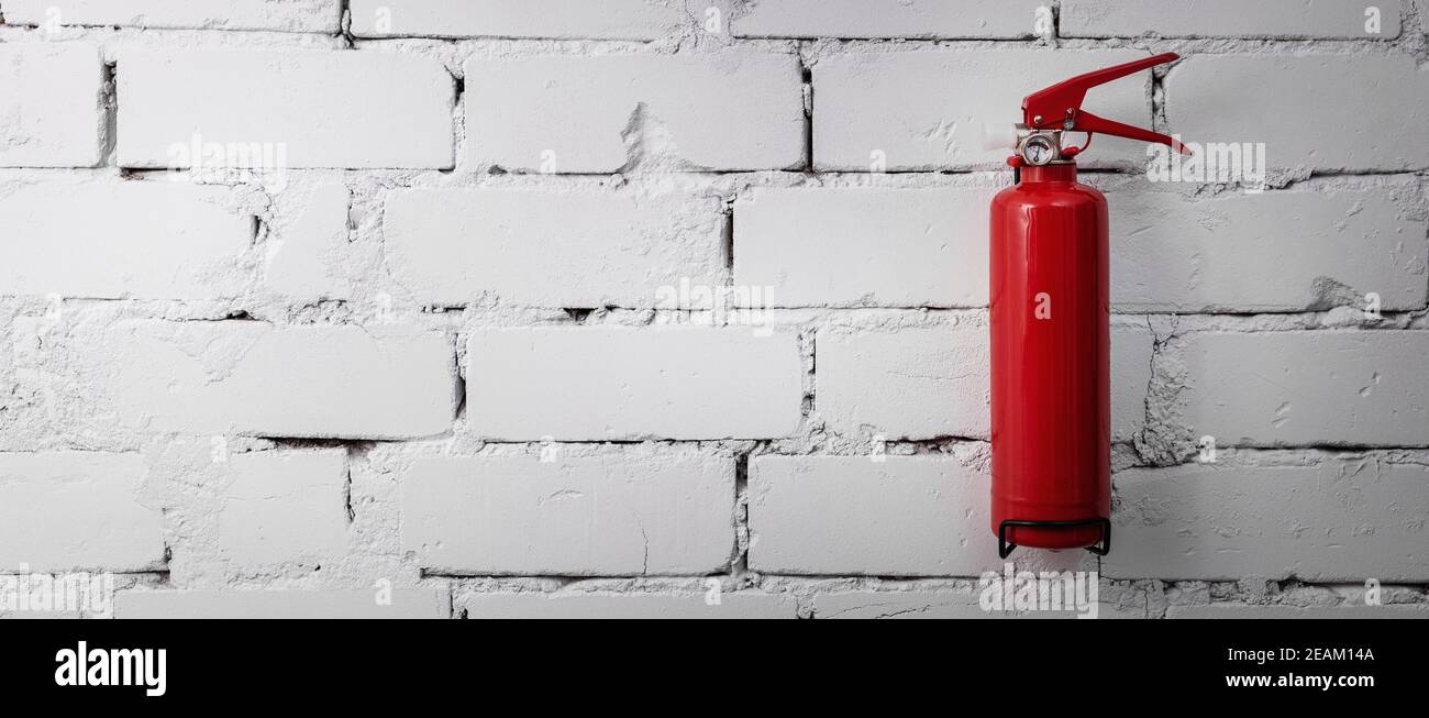 red fire extinguisher hanging on white brick wall. banner copy space Stock Photo