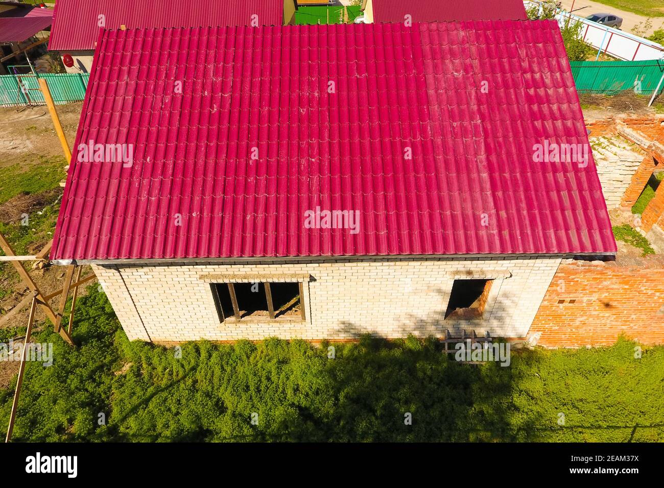 A house with a red roof made of corrugated metal sheets. Roof from corrugated metal profile. Metal tiles. Stock Photo