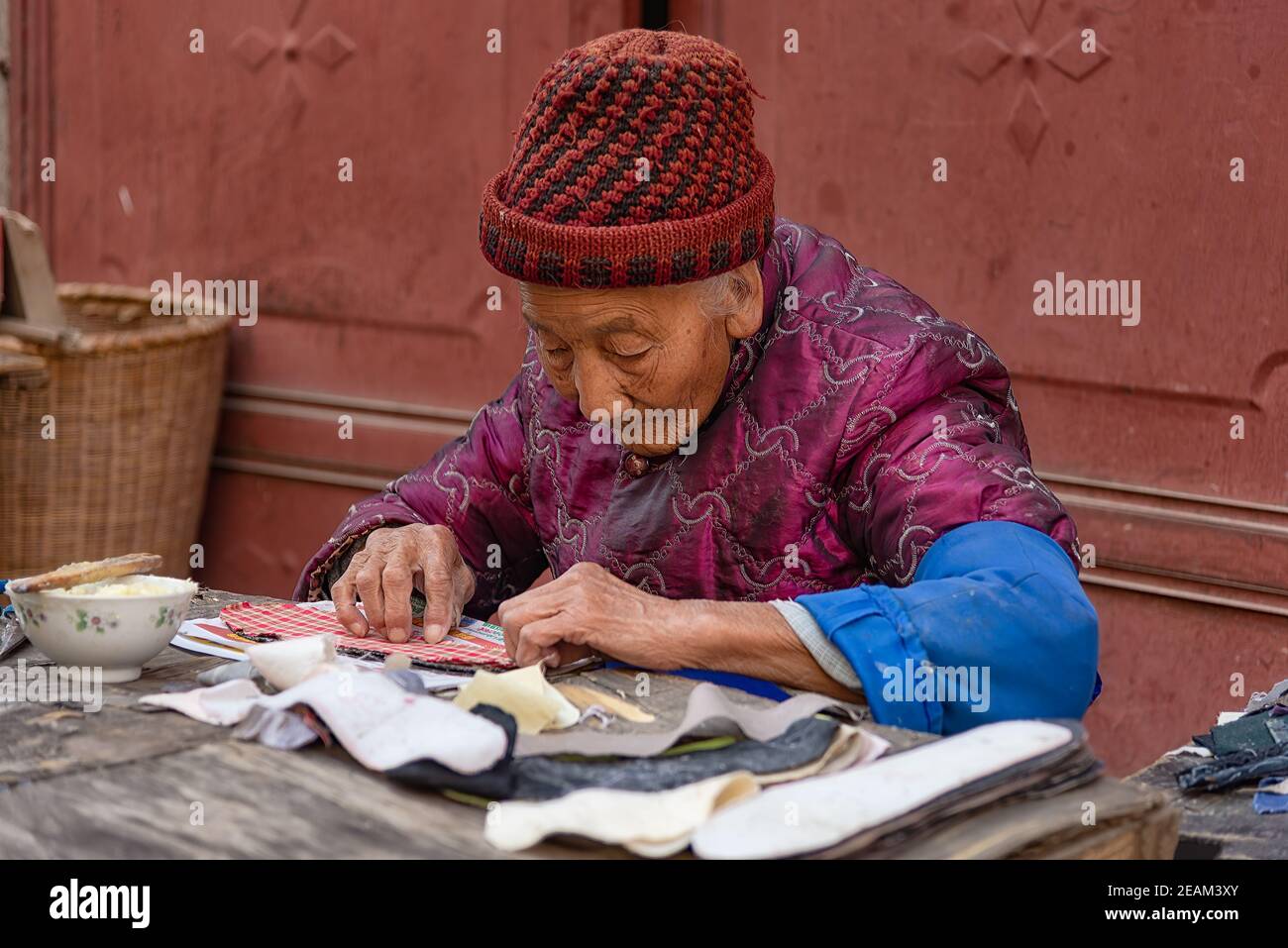 Xizhou, China - April 26, 2019: Portrait of an elderly woman at work at Xizhou old market. She's working on soles for the typical bai people shoes Stock Photo