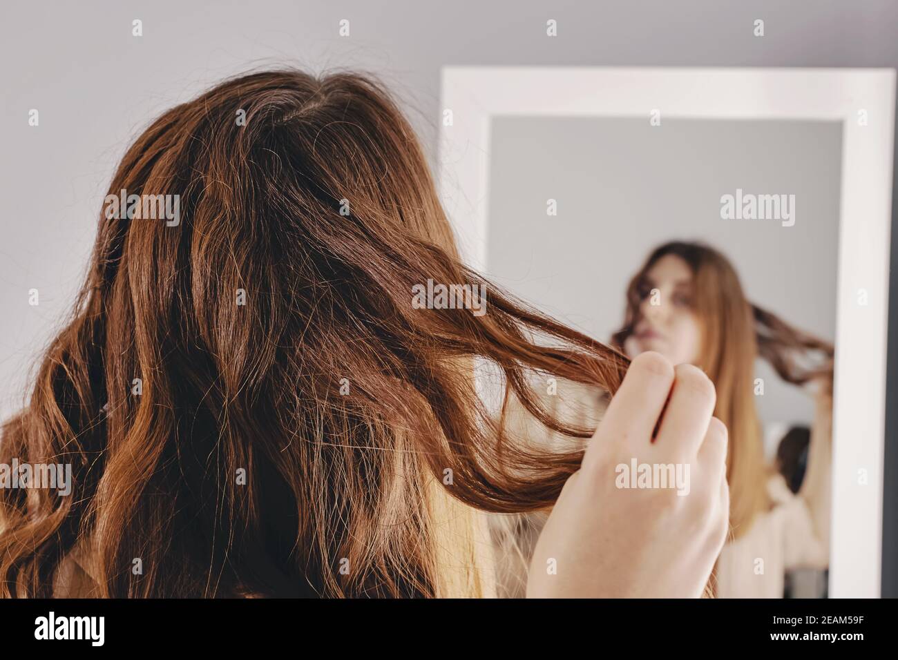 Young woman styling her shiny long brown hair Stock Photo