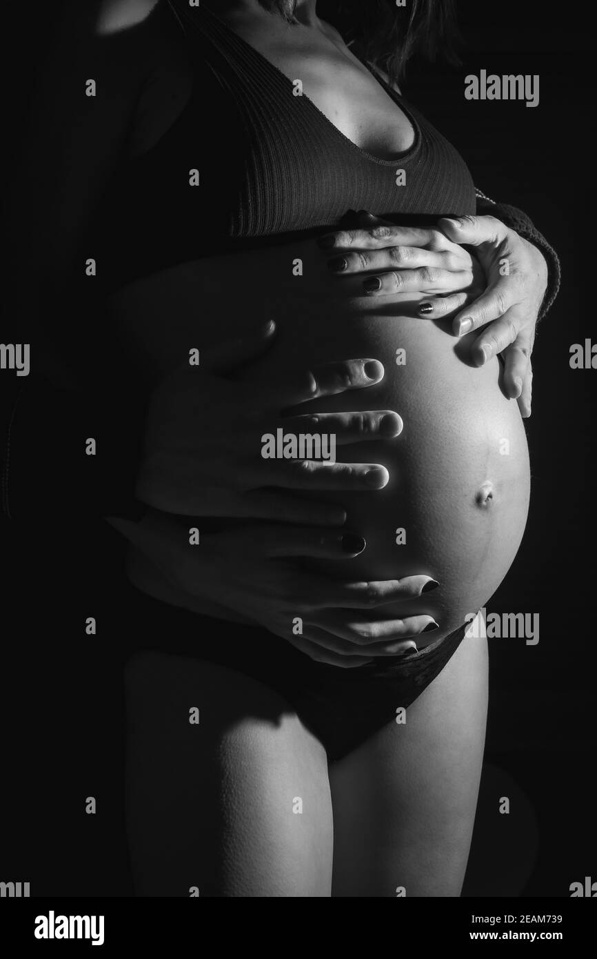 Grayscale vertical shot of a pregnant woman with the hands of her husband on her belly Stock Photo