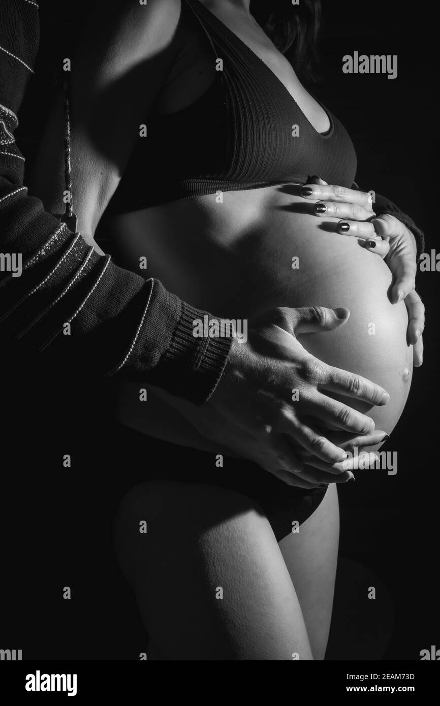 Grayscale vertical shot of a pregnant woman with the hands of her husband on her belly Stock Photo