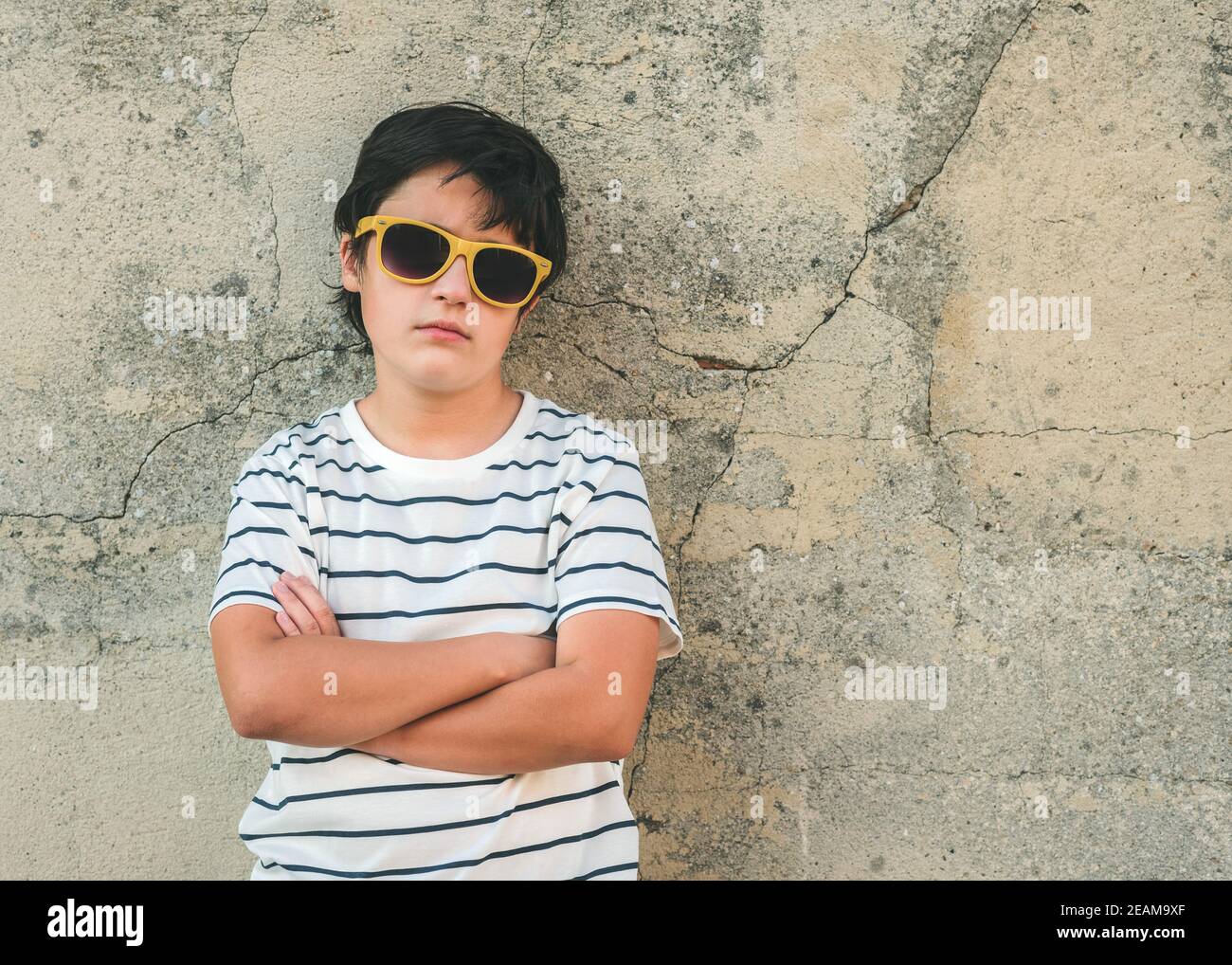 rebellious boy with sunglasses next to a wall outdoors Stock Photo