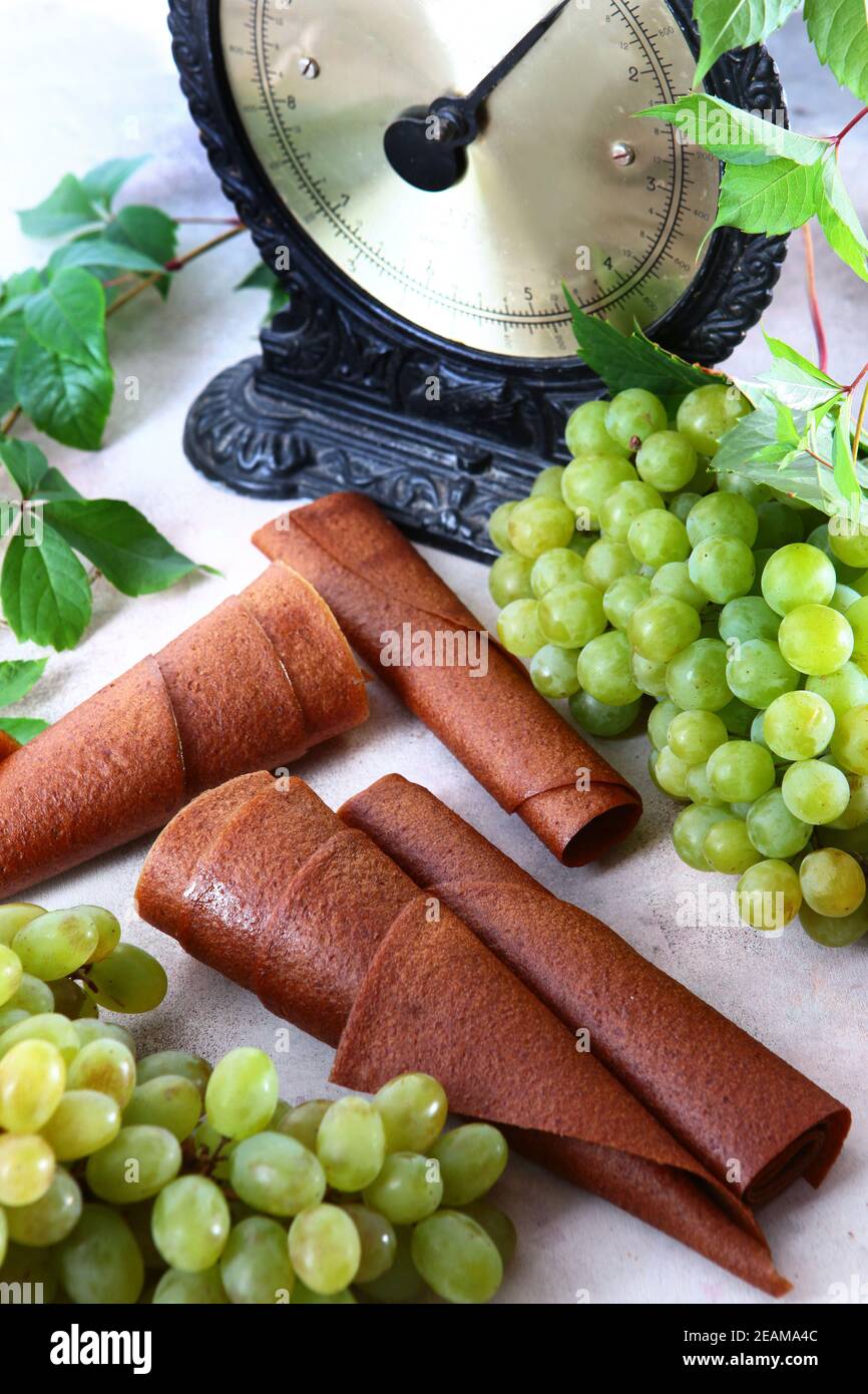 Natural light grape marshmallow is rolled into a tube. Natural bioproduct without preservatives. Vintage scales. Food for vegetarians. Photo on a light background. Vertical photo. Stock Photo