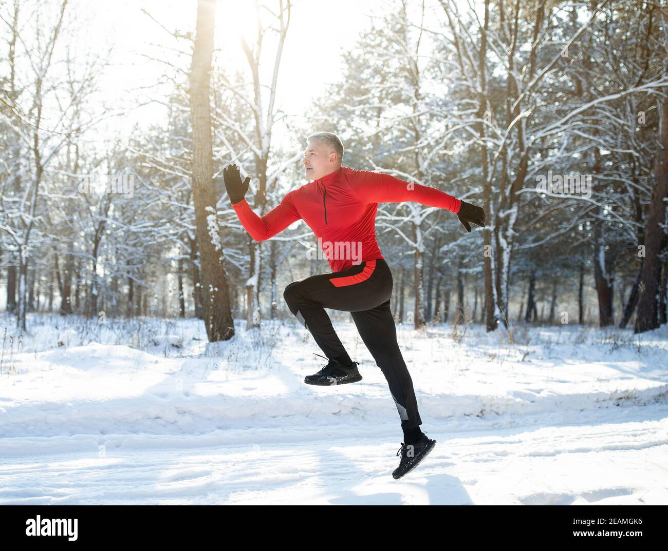 Full length portrait of strong mature sportsman jogging outside in sunny winter park. Seasonal sports and activities Stock Photo