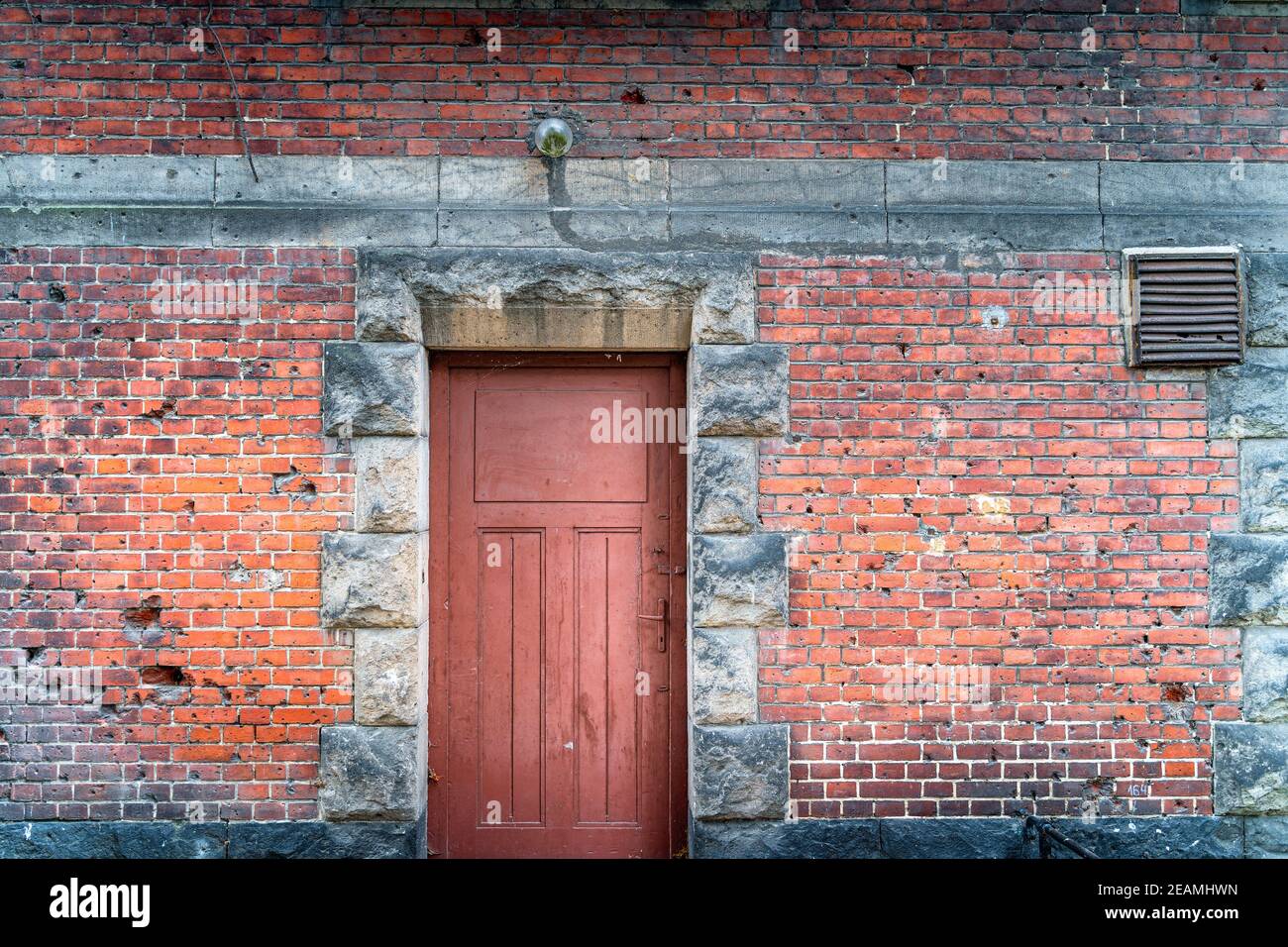 Bullet holes in a house facade from World War II. Rustic, red brick wall with doors Stock Photo