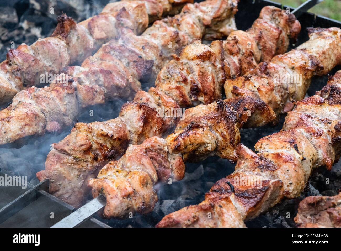 Frying pork on a skewer over a brazier. Turning meat over coals. Appetizing shish kebab. Stock Photo