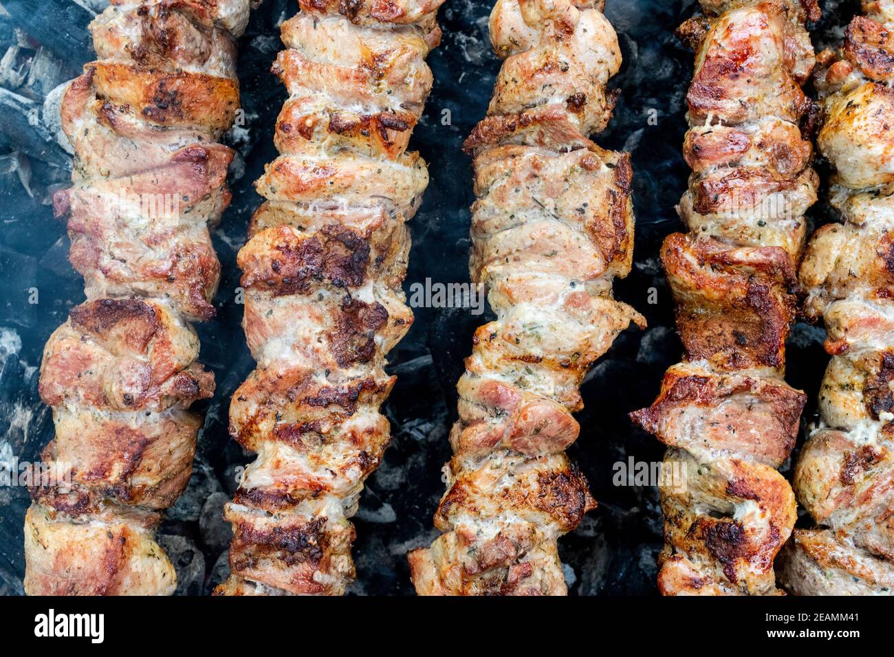 Frying pork on a skewer over a brazier. Turning meat over coals. Appetizing shish kebab. Stock Photo
