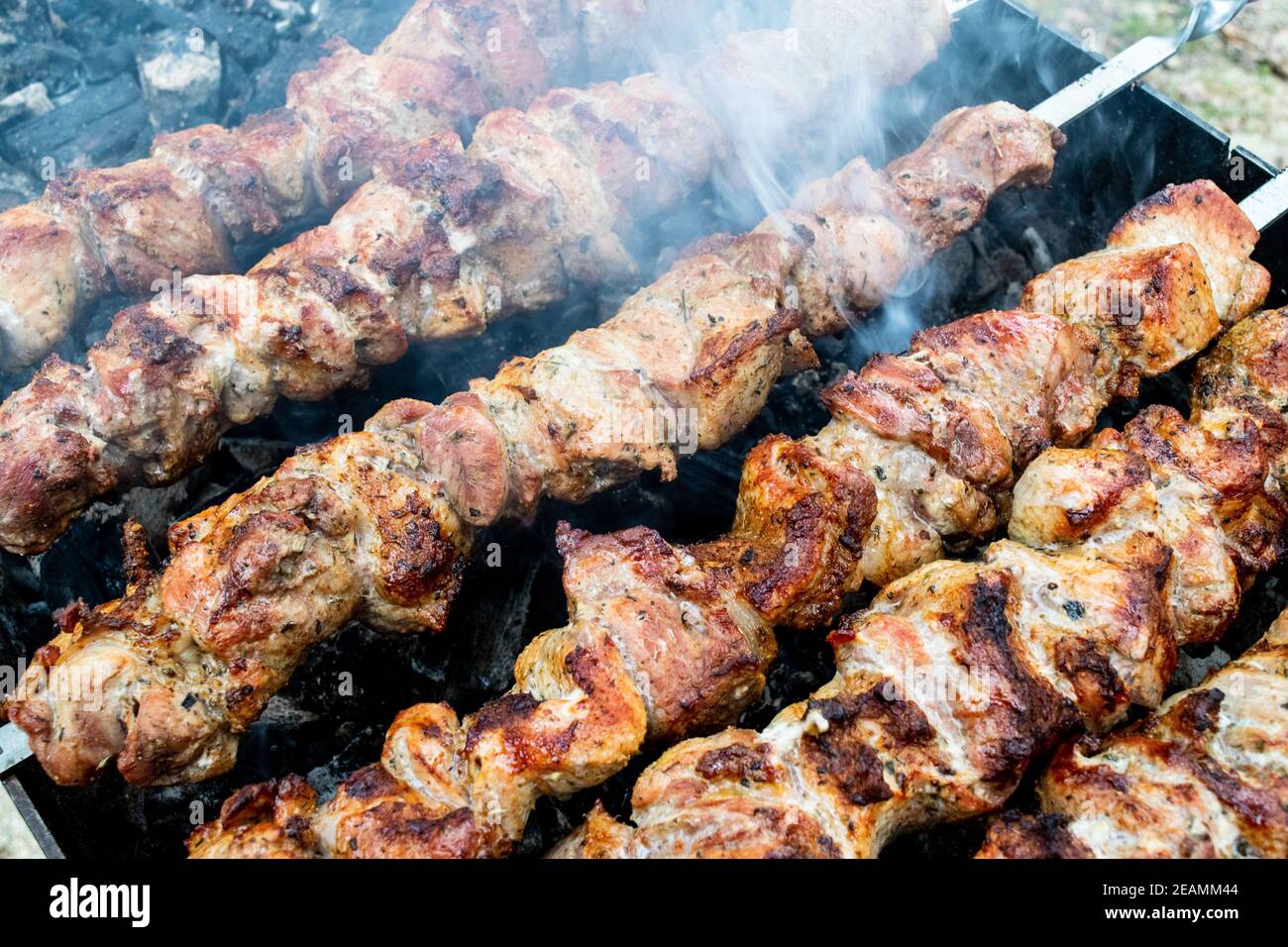 Frying pork on a skewer over a brazier. Turning meat over coals. Appetizing shish kebab. Stock Photo