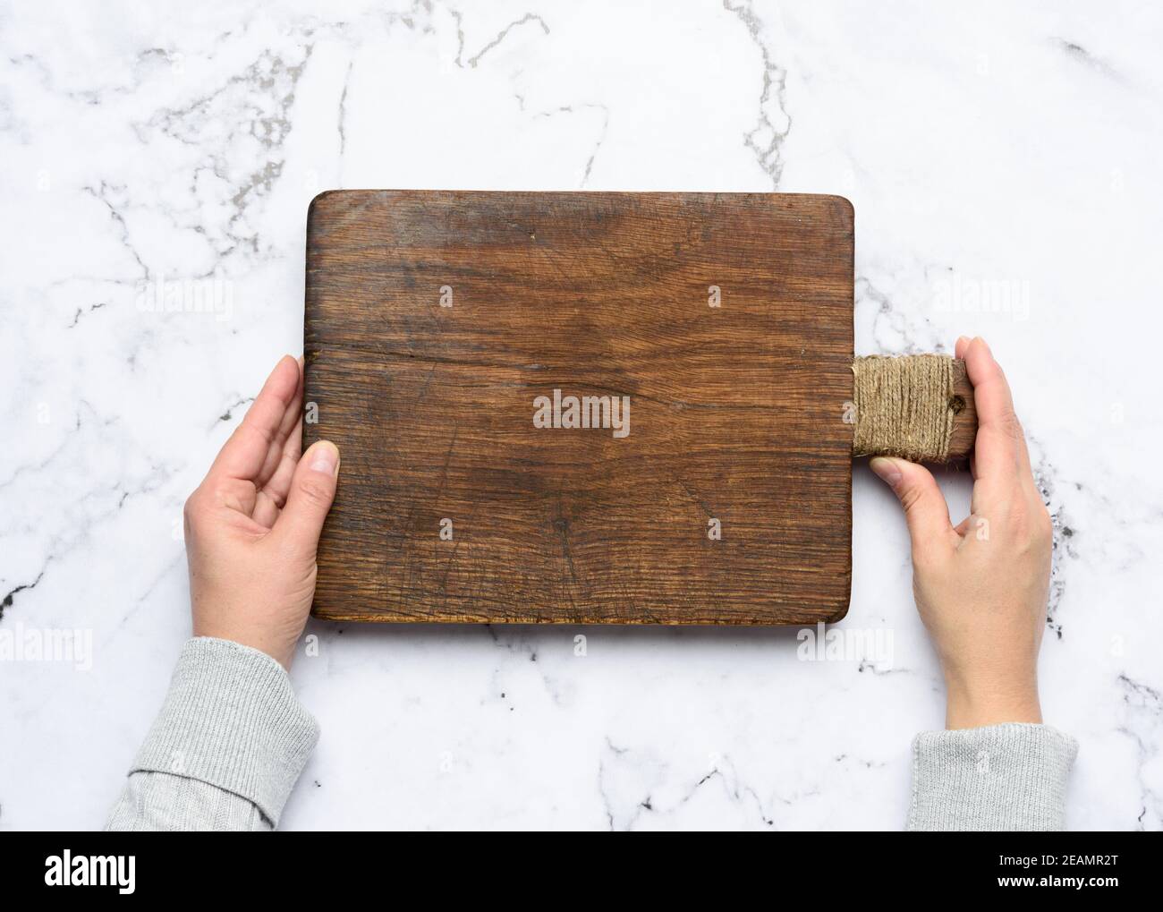 two female hands hold an empty old brown rectangular wooden cutting board Stock Photo
