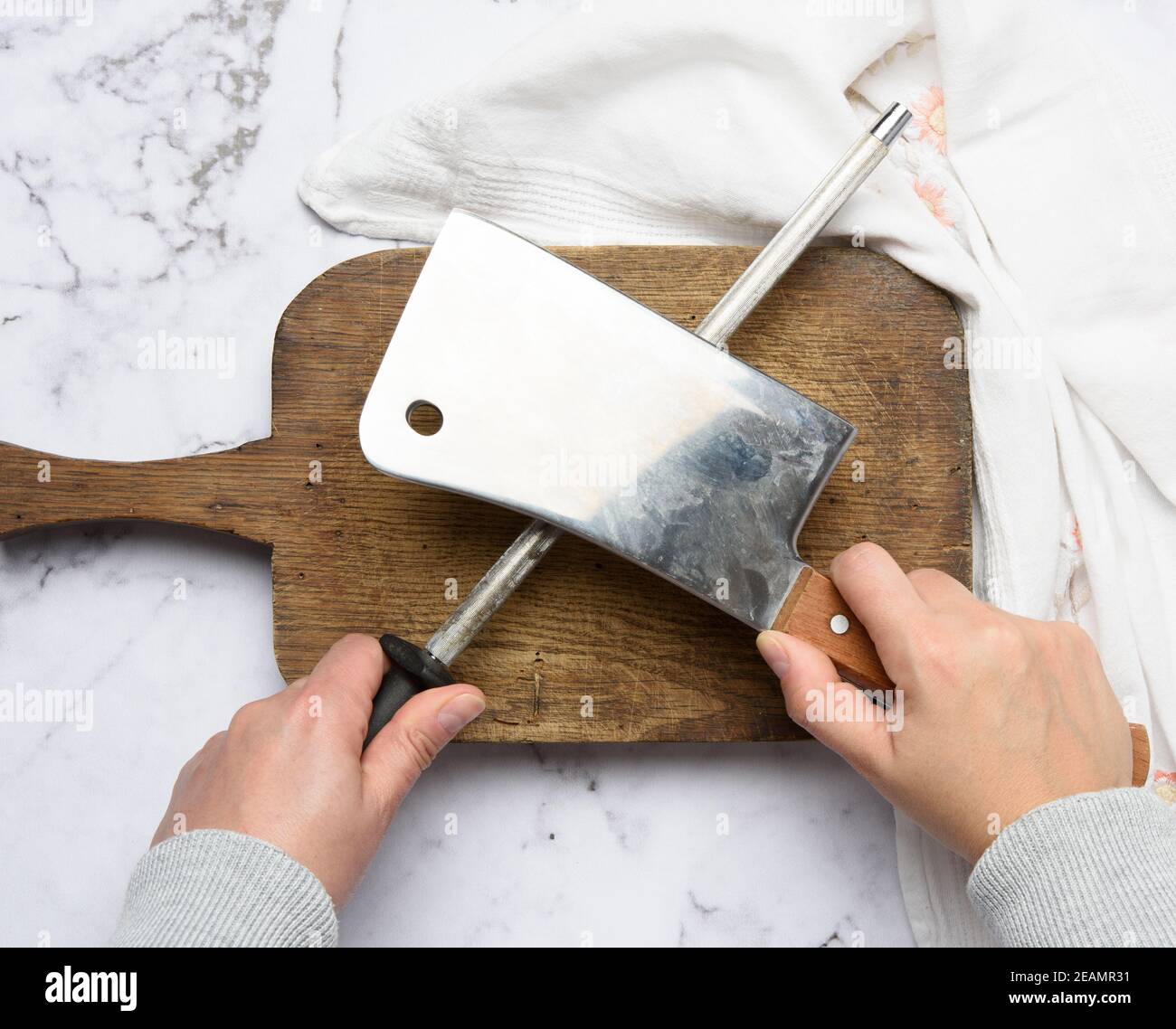 female hands hold a kitchen knife and a sharpener with a handle Stock Photo