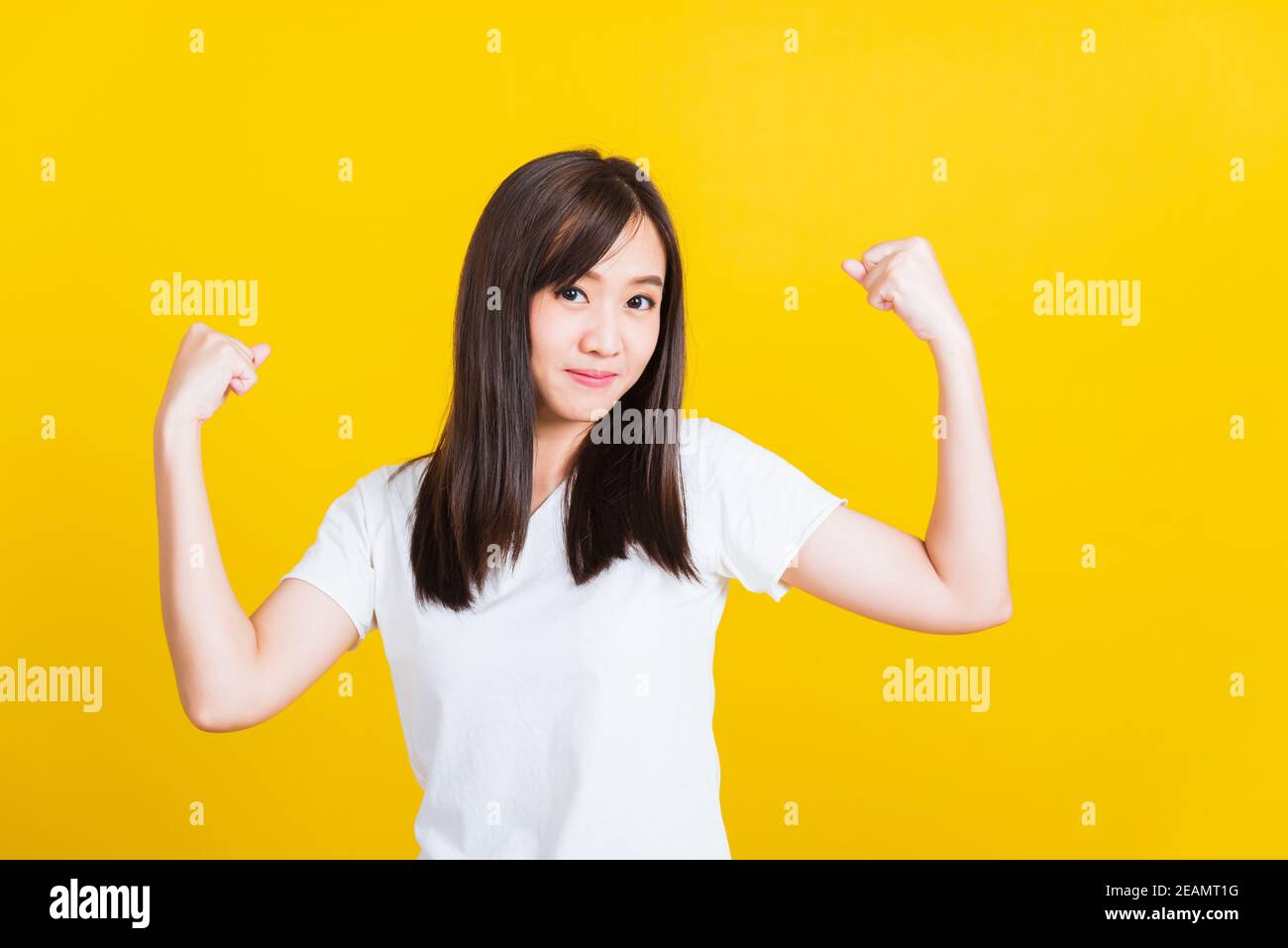 Young woman raises arms biceps confident showing power and strength Stock Photo