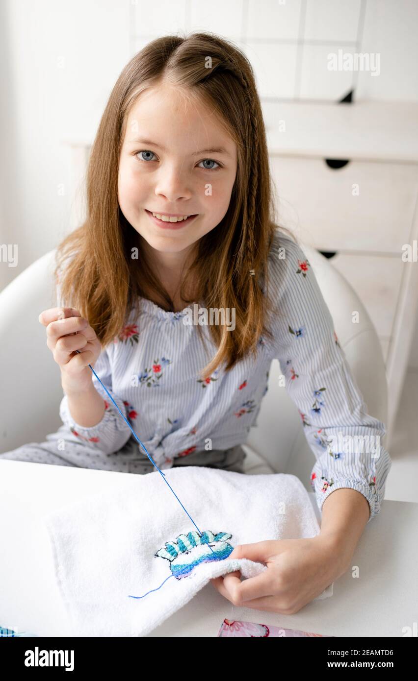 pretty and young schoolgirl is sitting by the table in her parents office embroidering, doing needlework Stock Photo