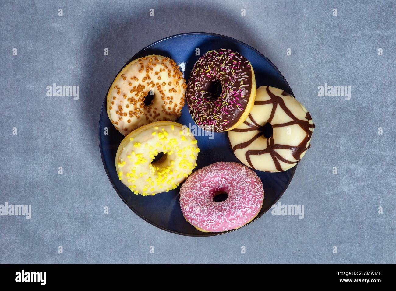 Colorful sweet glazed donuts with colored sprinkles on blue plate with ...