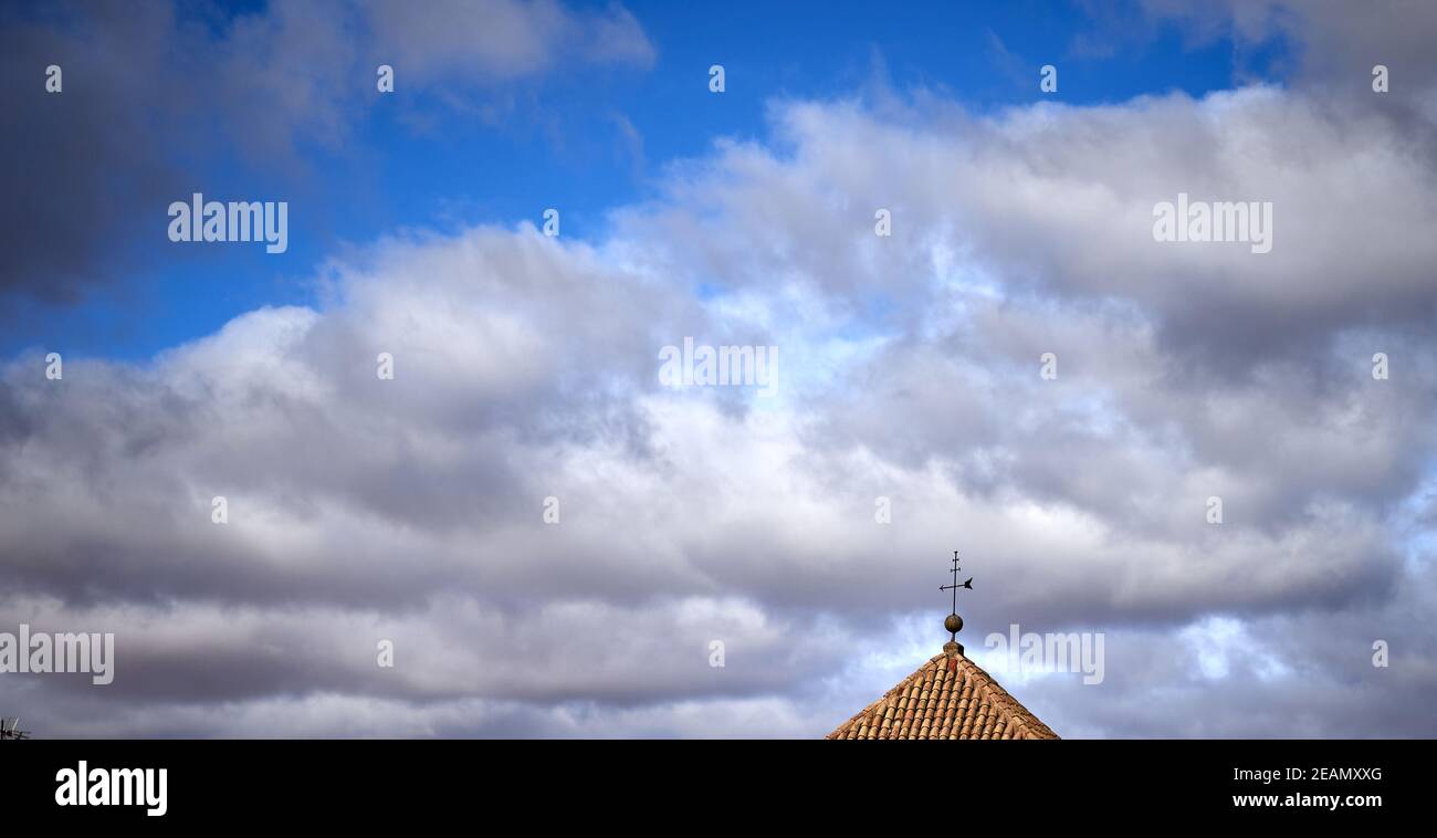 detail of a weather vane moved by the great wind on a hipped roof against a blue and cloudy sky Stock Photo