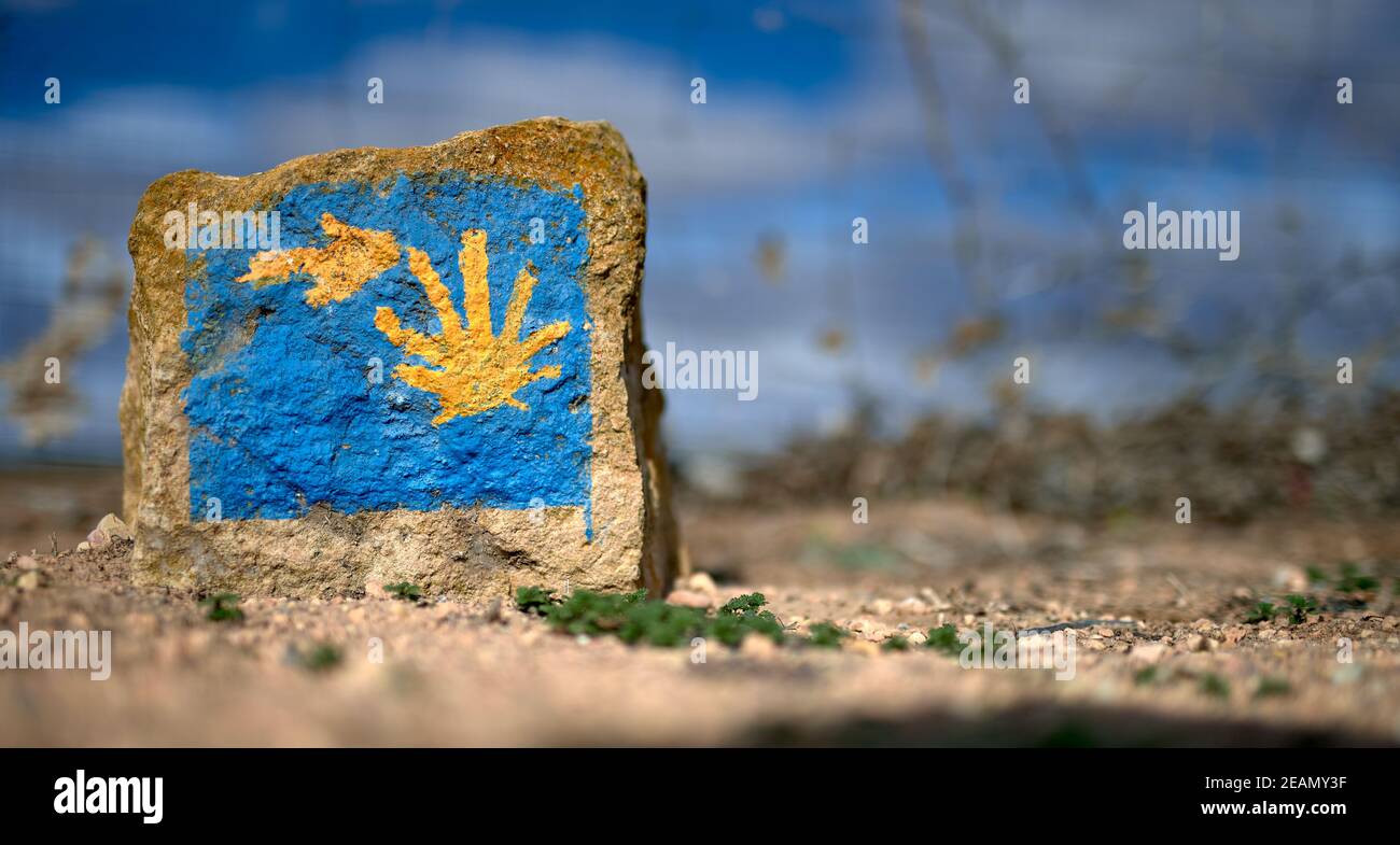 detail of a milestone representing the sign of the Way of St. James with an arrow and a yellow shell on a blue background Stock Photo