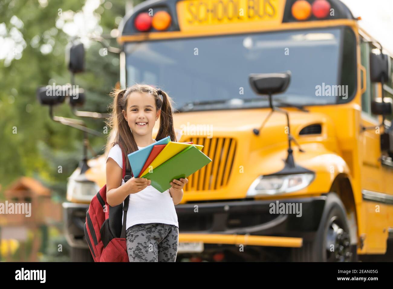 Girl with backpack near yellow school bus. Transport for students Stock