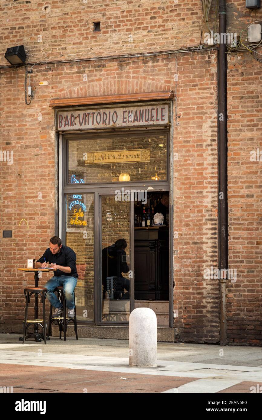 A man sitting oiutside a cafe, the Cafe Emanuelle, at a table writing  in Bologna Italy Stock Photo