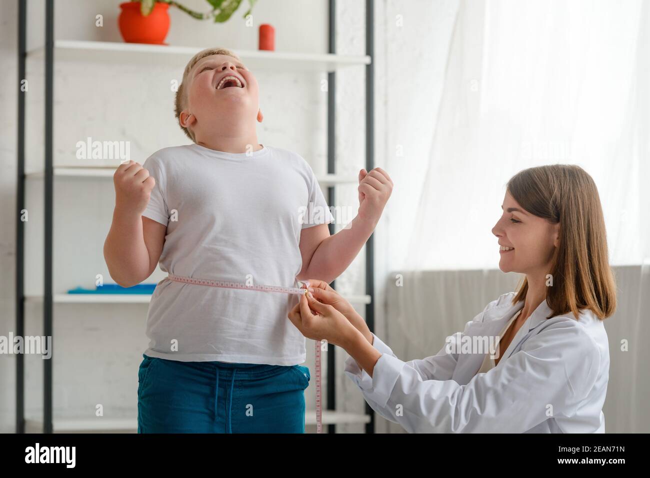 Boy excited to lose weight while happy nutritionist measuring his waist Stock Photo