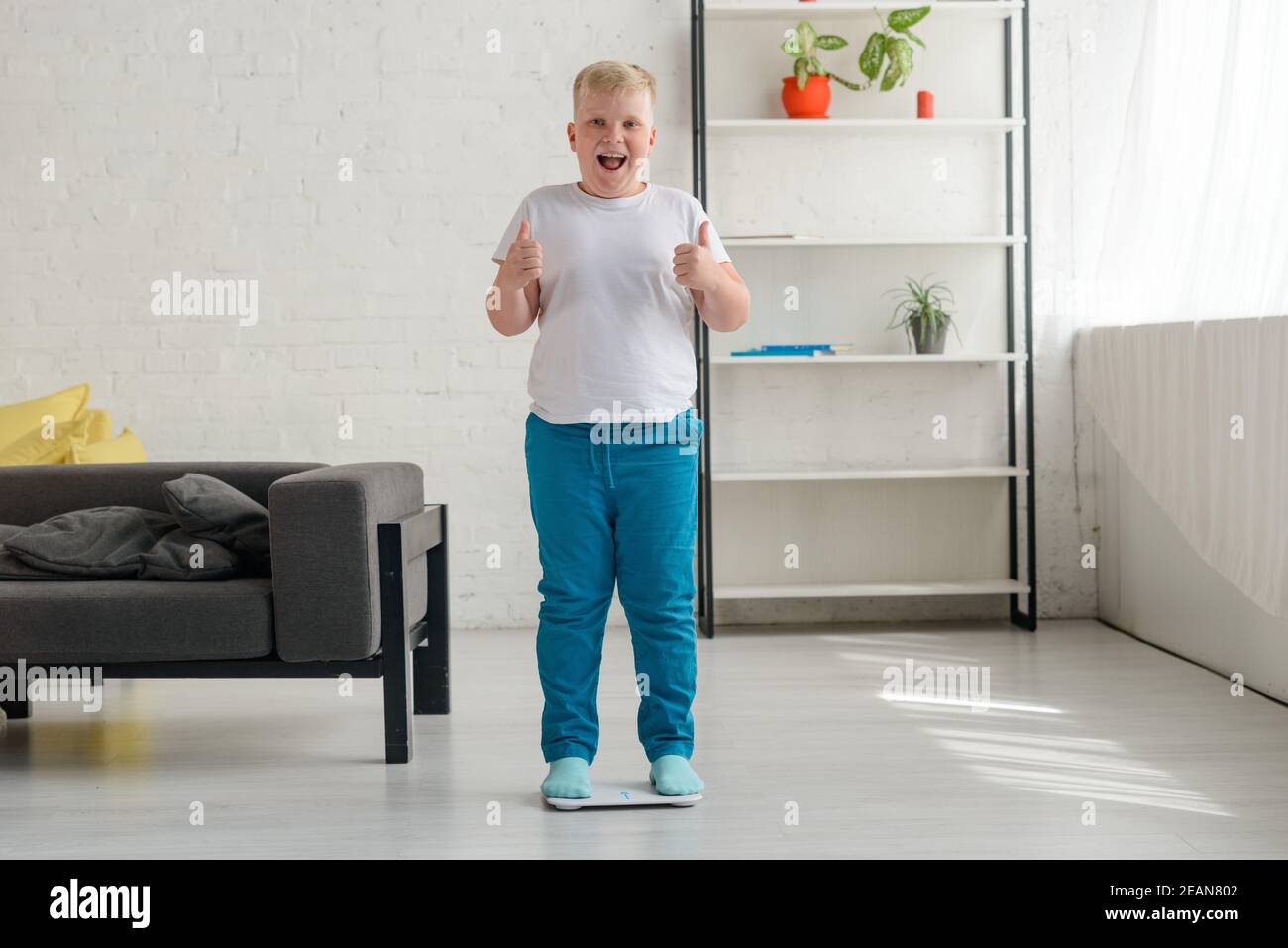 Happy overweight boy after weighing. Cheerful kid showing thumbs up Stock Photo