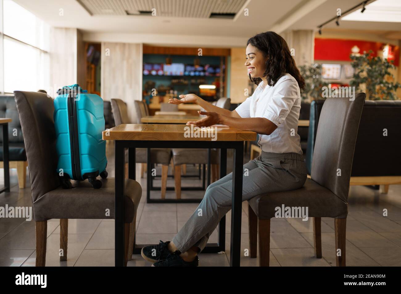 Woman with suitcase in cafe, airport waiting hall Stock Photo
