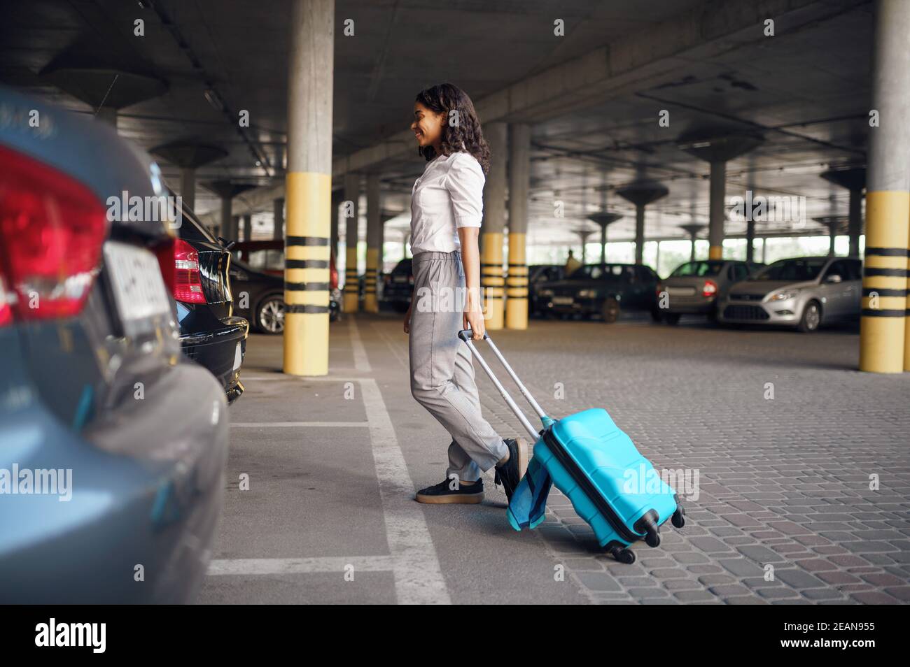 Young woman with suitcase in car parking Stock Photo