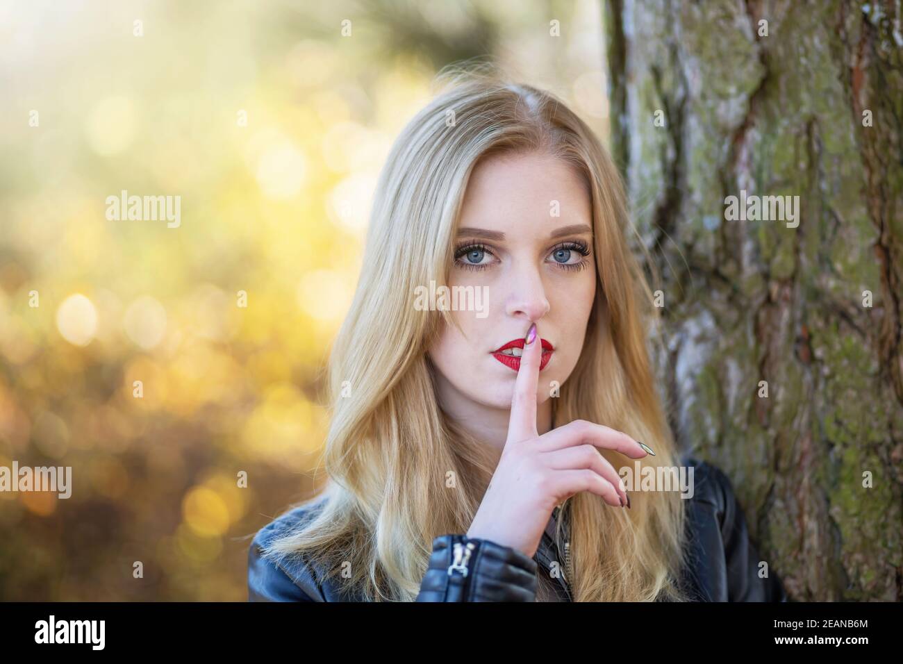 Attractive long hair girl is gesturing Shhh posing in autumn park. Horizontally. Stock Photo