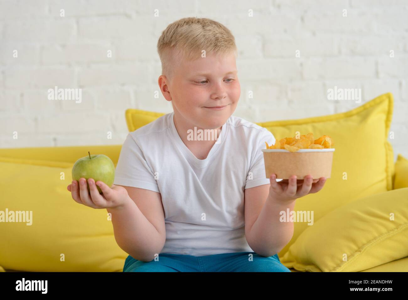Fat boy choosing between an apple and chips Stock Photo