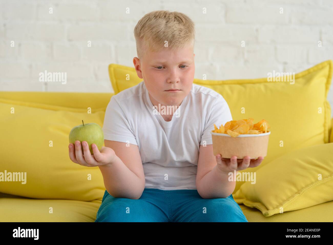 Obese boy choosing between foods. Apple or chips Stock Photo