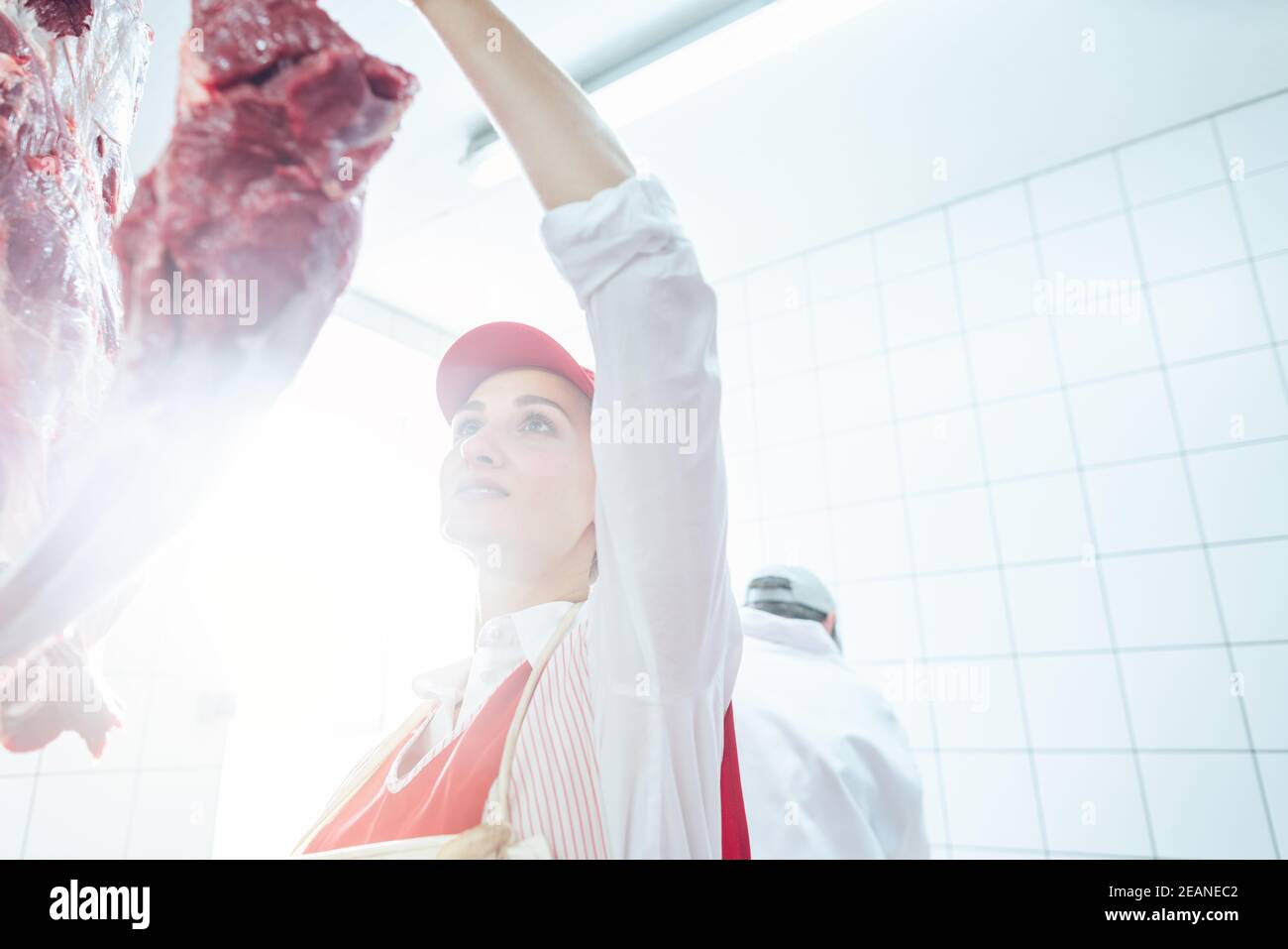 Butcher woman taking meat from hook to cut and sell it Stock Photo
