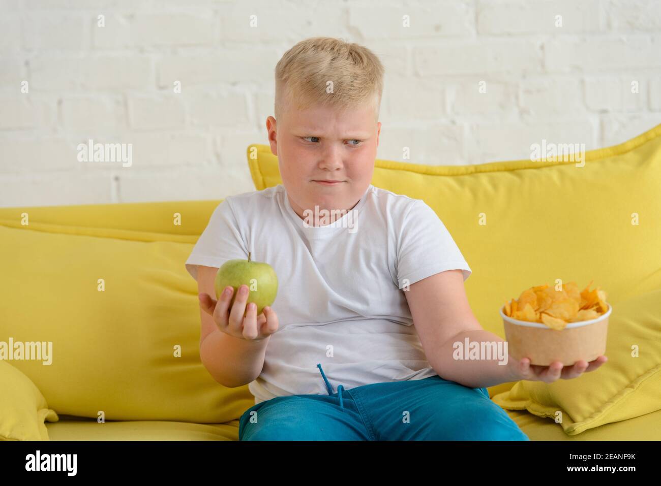 Boy holding apple and chips, and can't decide what to eat Stock Photo