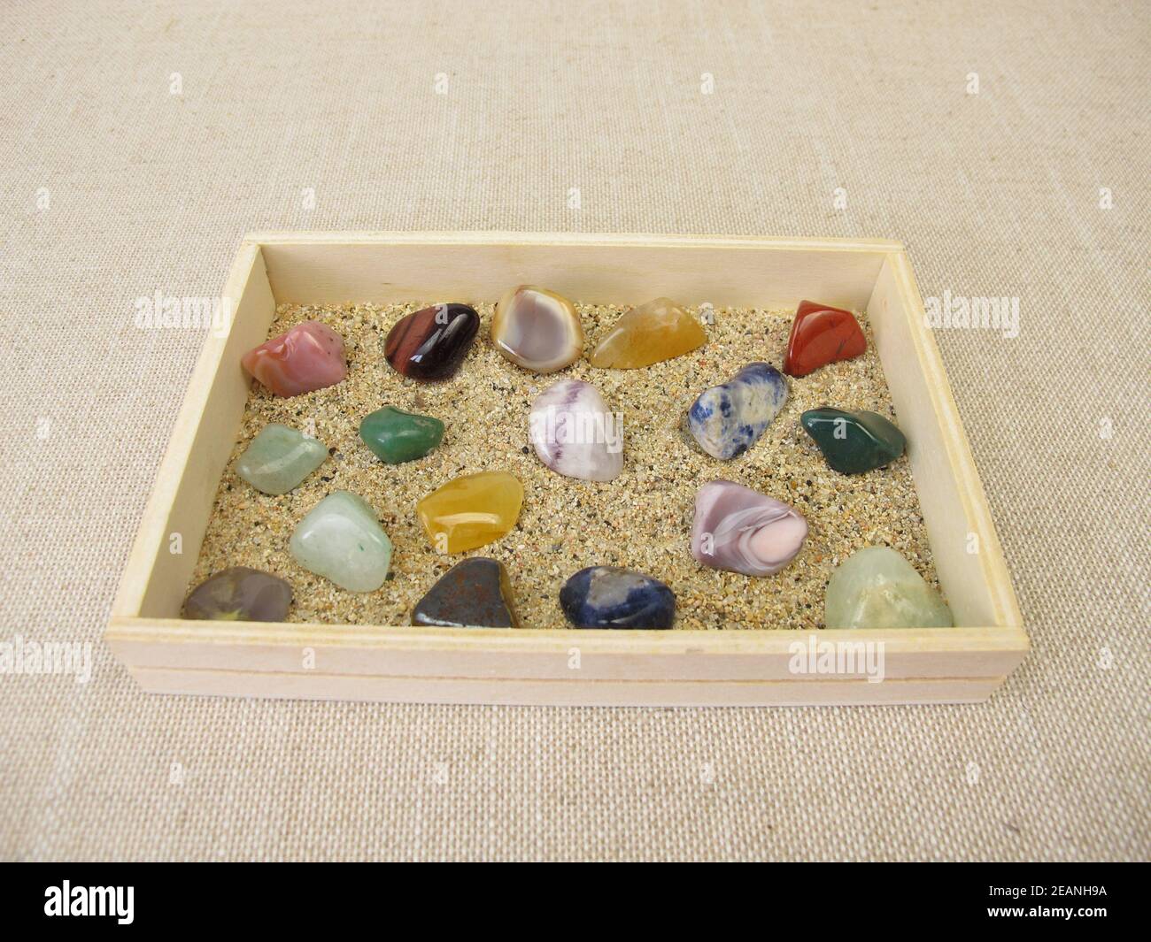 Tumbled gemstones in a wooden box with sand Stock Photo