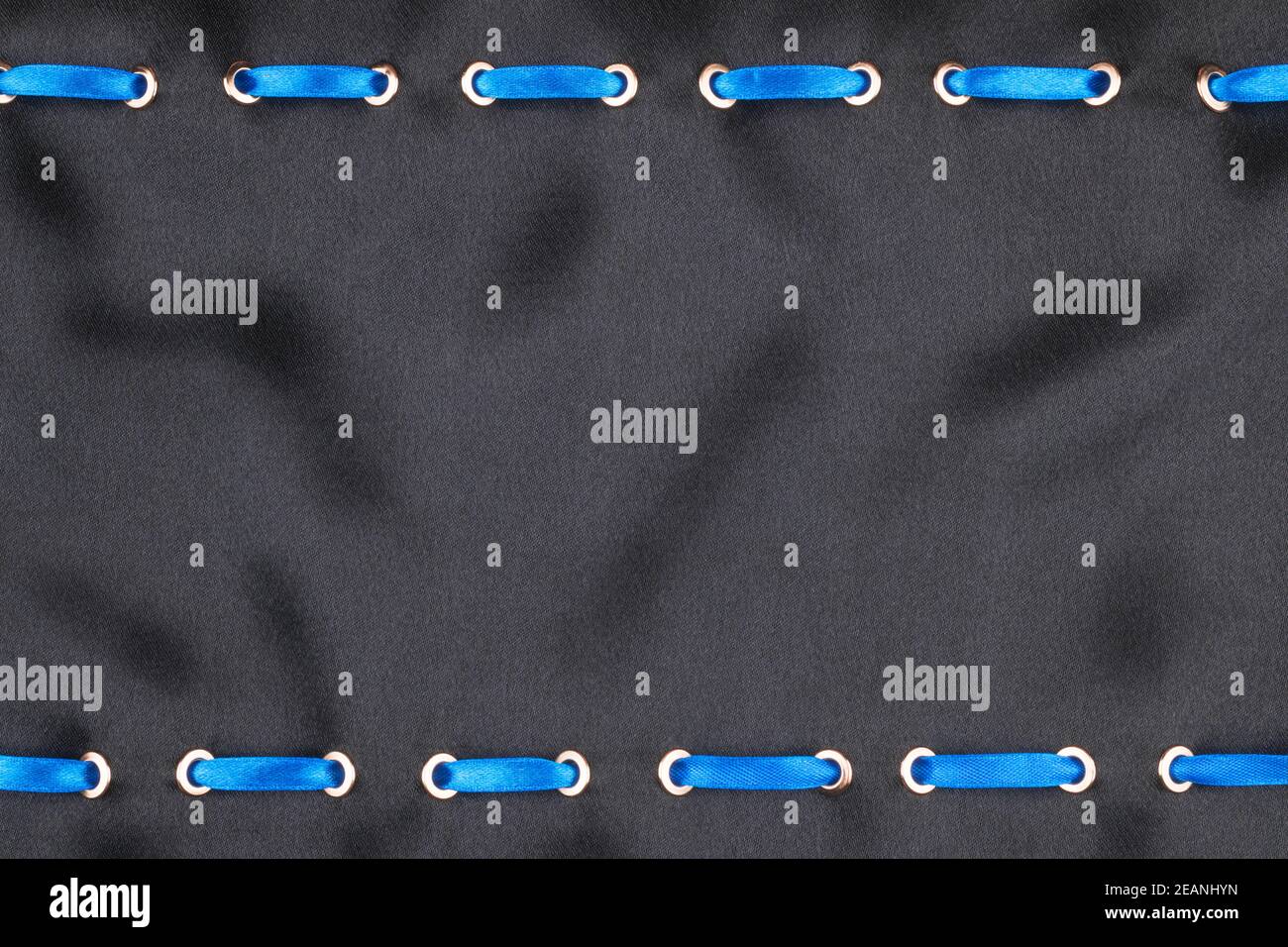 Blue satin ribbon inserted in the gold rings on black silk Stock Photo