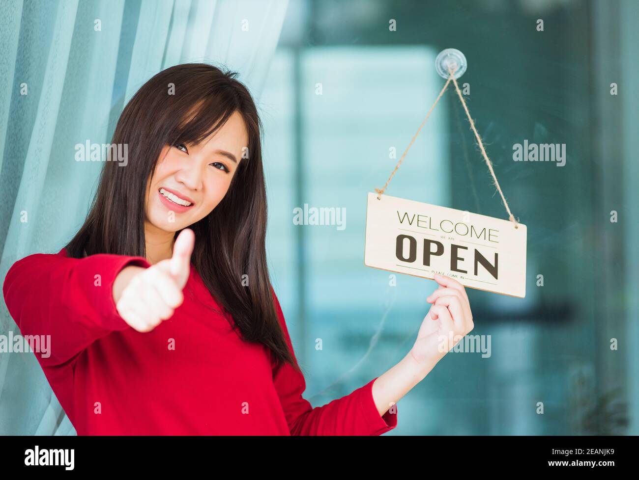 Woman smile show finger thumb up for good sign she notice sign wood board label 'WELCOME OPEN' hang through glass door front shop Stock Photo