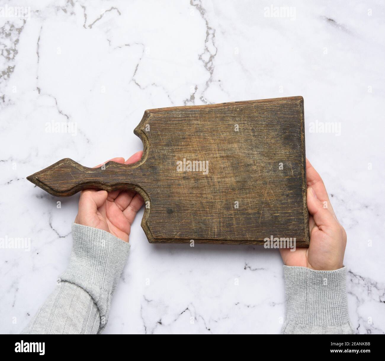 two female hands hold an empty old brown rectangular wooden cutting board Stock Photo