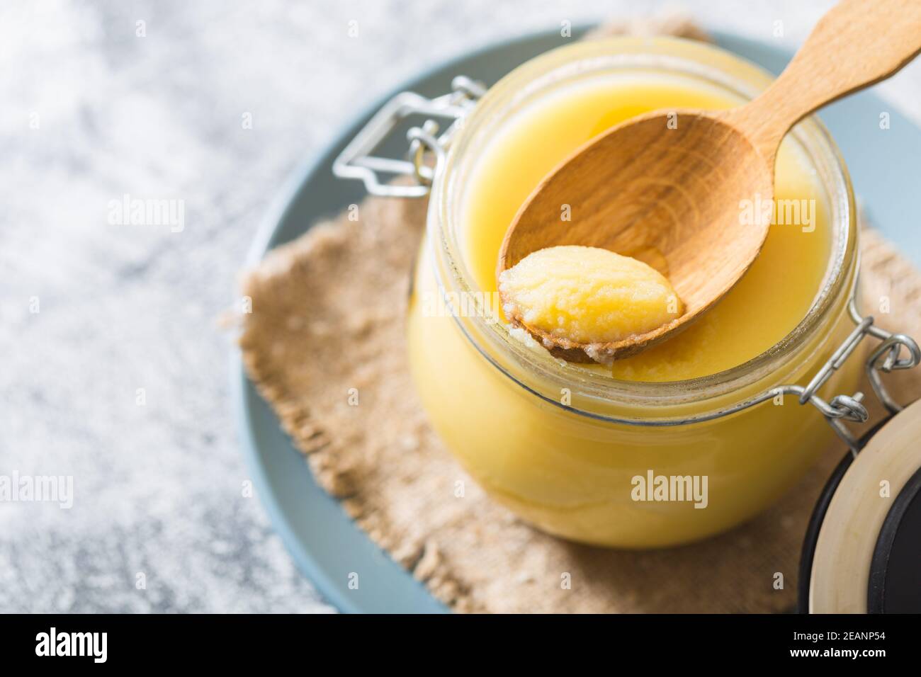 Ghee or clarified butter in jar and wooden spoon on gray table. Top
