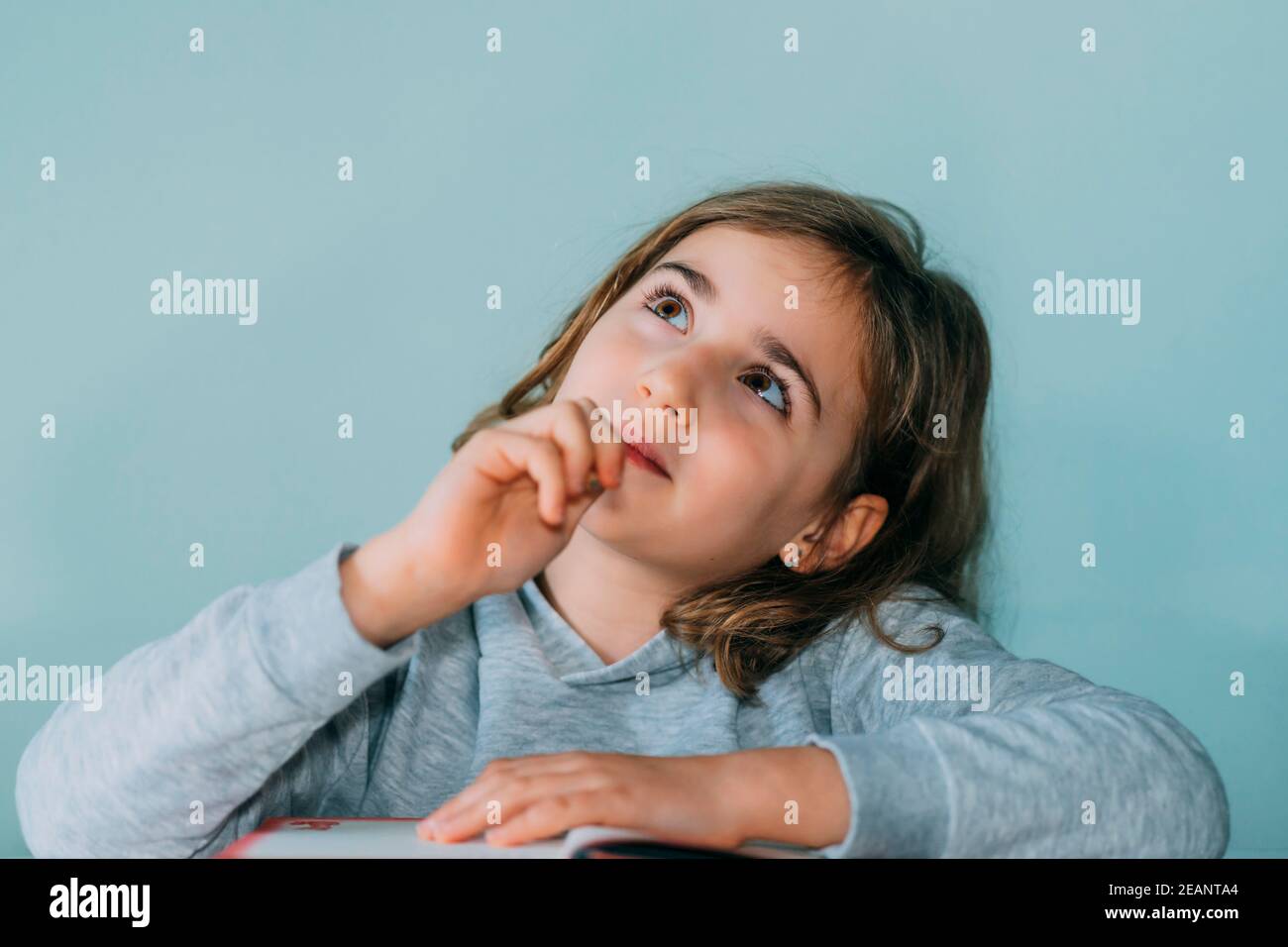 adorable little girl thinks of an idea while biting the pencil, looks up. Age 7 to 9 years, horizontal Stock Photo