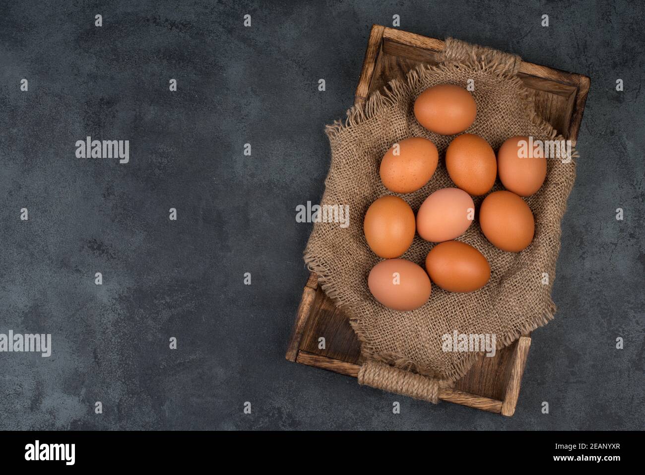 Brown raw chicken eggs in a wooden basket on a grey textured background ...