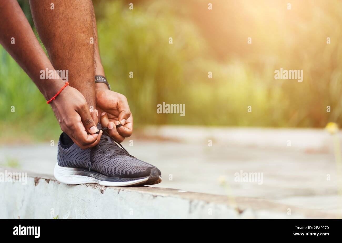 runner black man wear watch stand step on the footpath trying shoelace running shoes Stock Photo