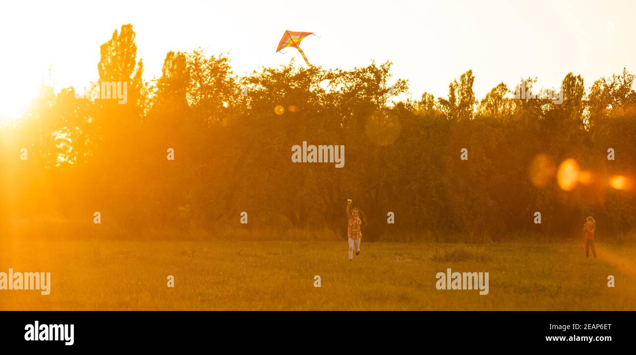 Two kids flies a kite over sunset in park Stock Photo